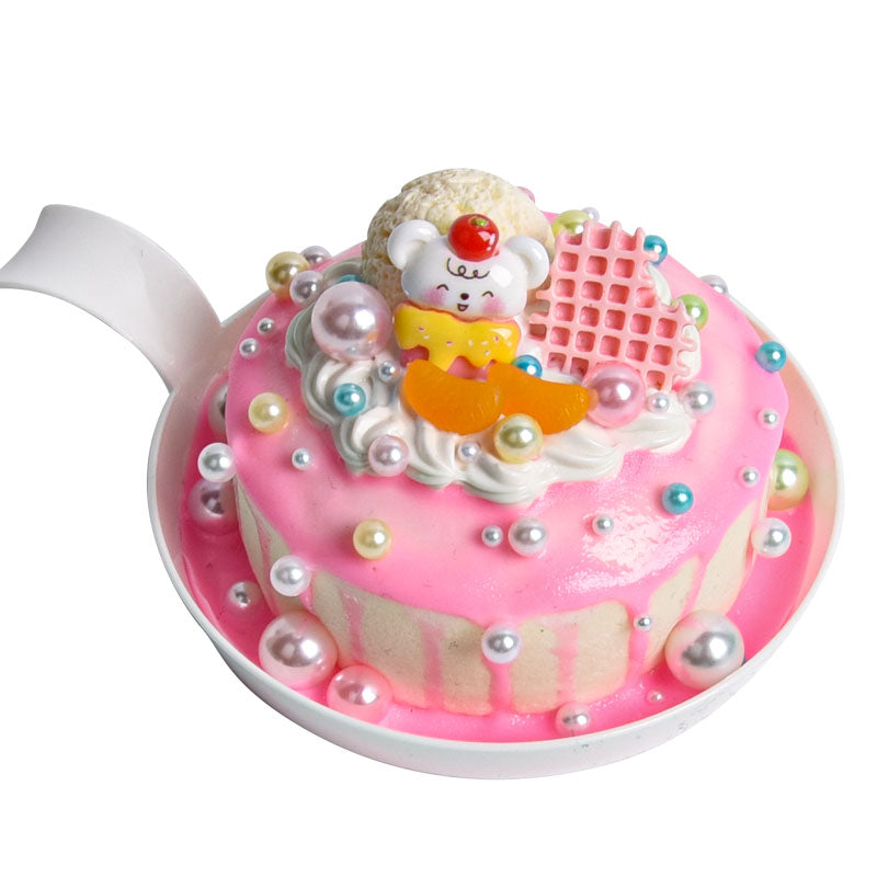 Decorative cake with a teddy bear figure on top, placed inside a teapot.