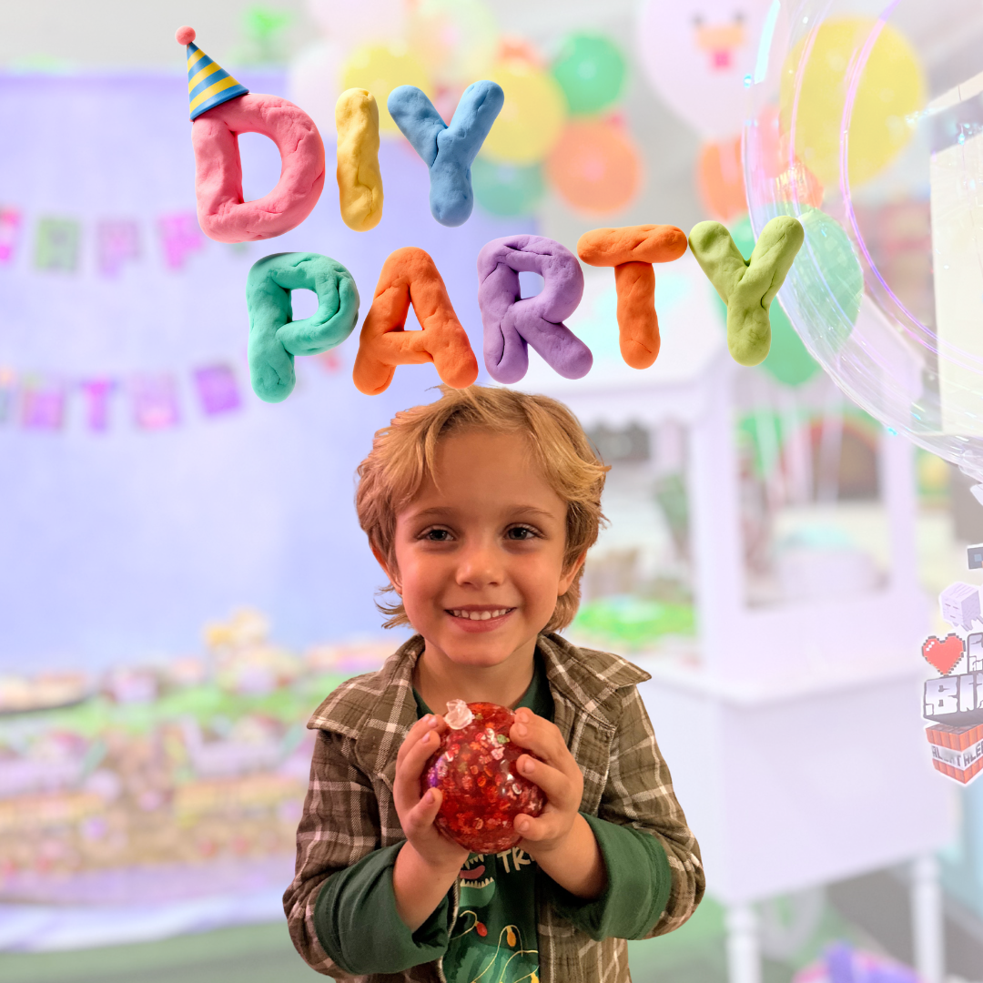 Child holding a red decorative ball at a DIY party with colorful letter decorations.