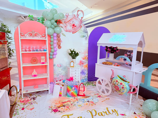 Children's tea party setup with pink shelves, balloons, and a white tea cart.