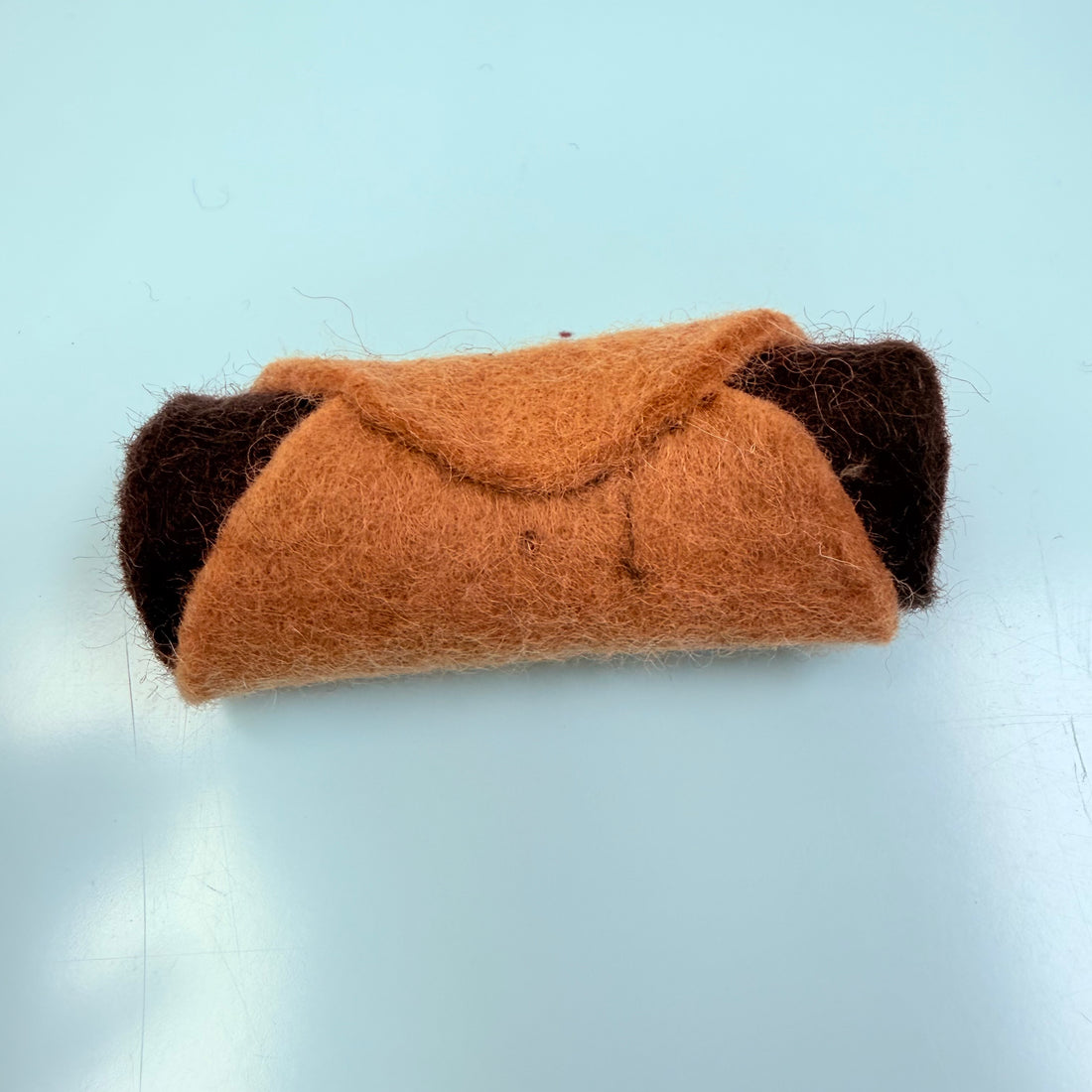 Felted brown and black cat-shaped object on a light blue background