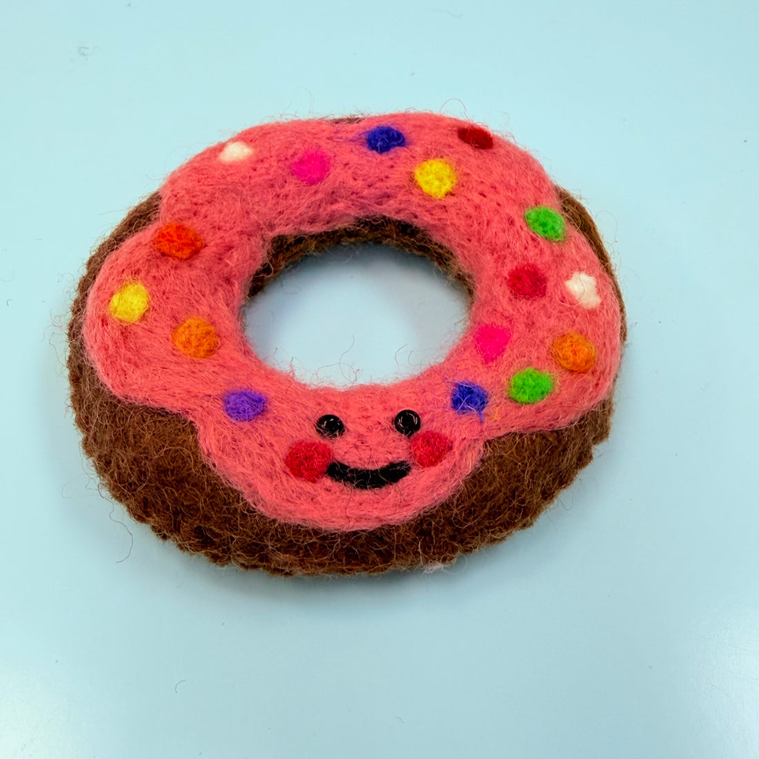 Felted donut toy with pink icing and colorful sprinkles