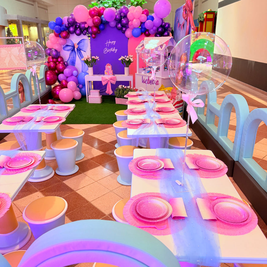 Children's birthday party setup with pink and purple decorations, balloons, and tables.