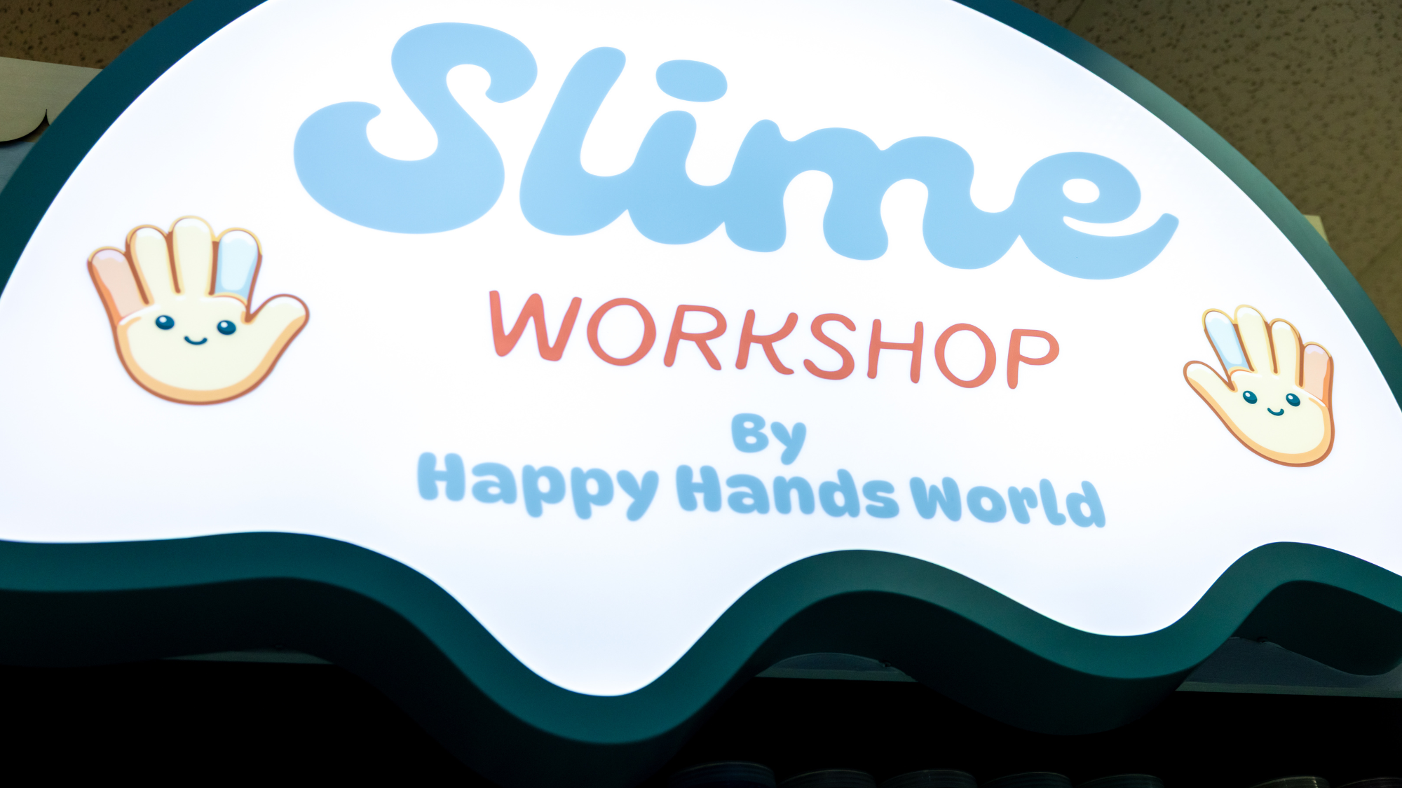 Advertisement for a slime workshop by Happy Hands World with cartoon hands on a wavy background.