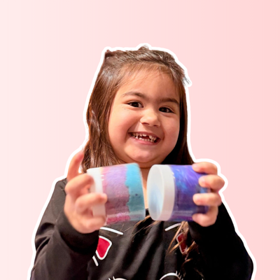 Child holding two colorful cylindrical objects against a pink background